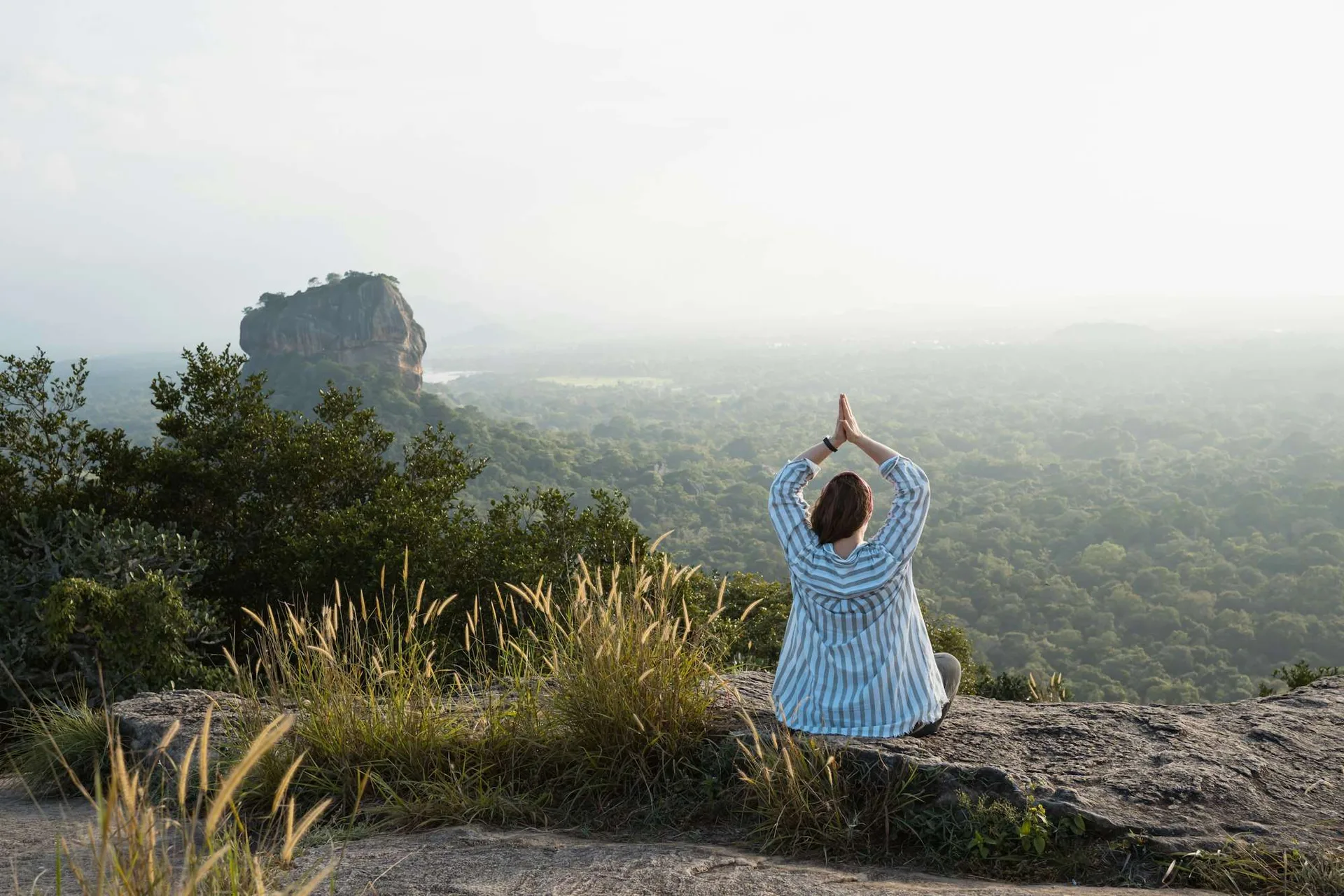 Traveller doing yoga at sunset with Sigiriya rock in the distance